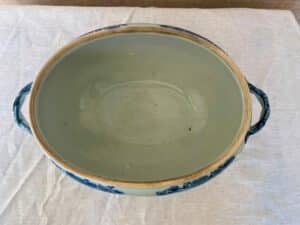 An empty blue and white ceramic bowl with two handles on a white tablecloth.