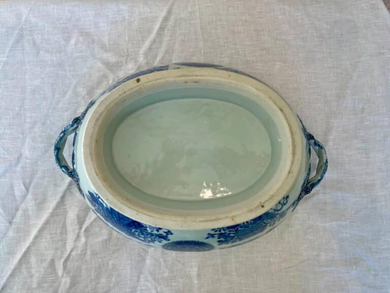 An overhead view of an empty, oval ceramic dish with blue floral patterns and side handles, placed on a white textured cloth.