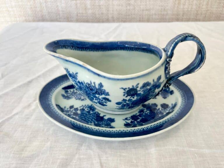 A blue and white floral-patterned gravy boat with a matching saucer on a white tablecloth.