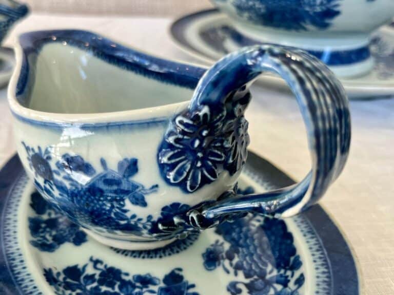 Close-up of a blue and white porcelain creamer with floral patterns, resting on a matching saucer.