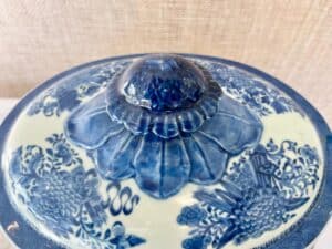 Close-up of a blue and white ceramic lid with floral and bird patterns, featuring a knob shaped like a flower.