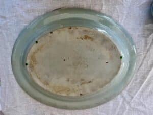 An oval-shaped ceramic dish with a pale green rim and a worn, speckled base lies on a white cloth.