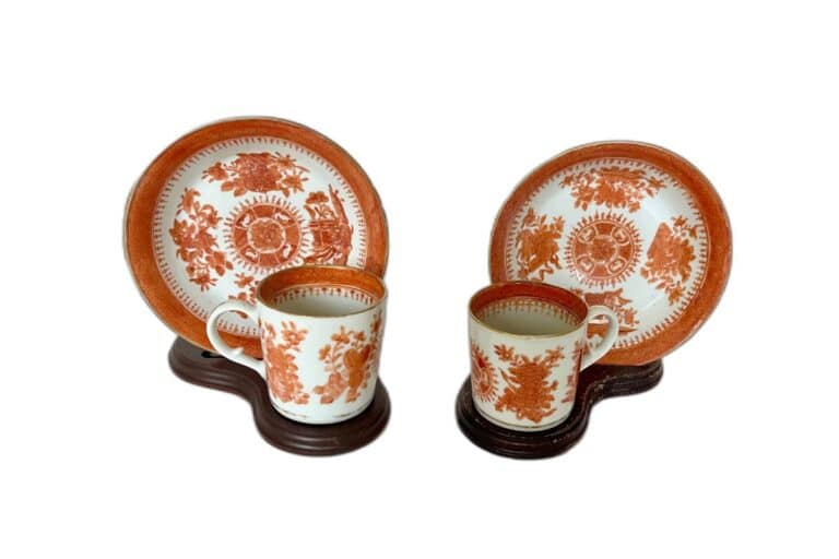 Two matching ceramic cup and saucer sets with red and white floral patterns, each on a separate wooden stand.