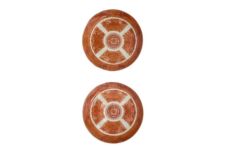 Two round, decorative wooden plates with intricate, symmetrical patterns in red and cream tones, placed one above the other against a white background.