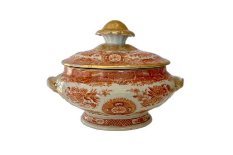 A decorative porcelain tureen with a lid, featuring red and gold floral patterns and handles on each side.