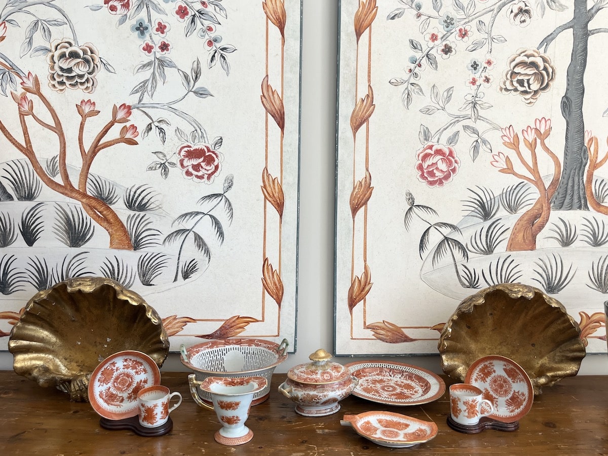 Collection of ornate red and gold dishware displayed on a wooden surface, set against a decorative floral-patterned backdrop.