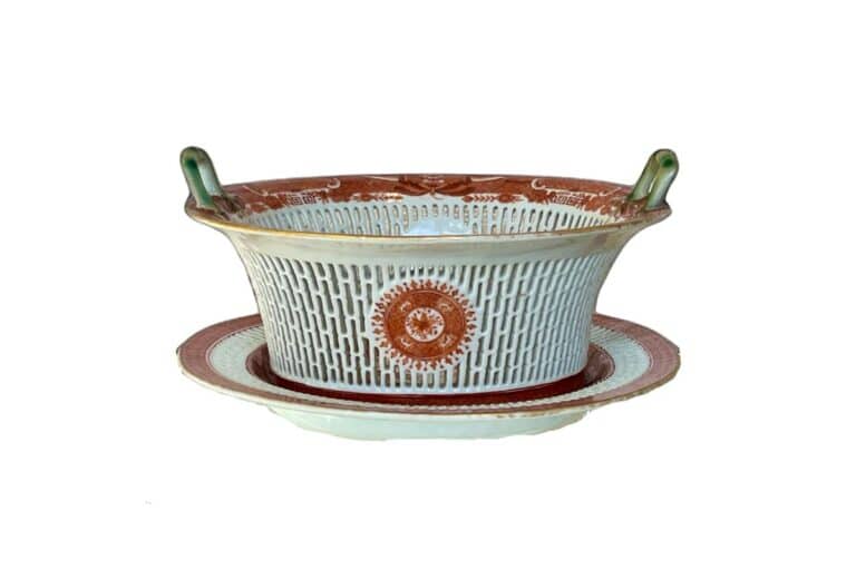 A decorative ceramic bowl with handles, featuring intricate red and white patterns, rests on a matching plate.