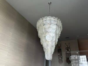 A spacious room with textured walls and decorative wall art features a tiered Murano Glass Chandelier, purchased in Paris, elegantly hanging from the ceiling. Its translucent, oval glass pieces add a modern touch to the decor.