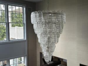 The Murano Glass Chandelier, purchased in Paris, hangs with a modern teardrop design in a room featuring large windows and neutral-colored walls.