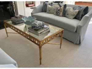 Living room with a pair of Niermann Weeks Tight Back Blue Sofas, adorned with patterned pillows, and featuring a glass-top coffee table accented with gold trim. Books and a decorative bowl are neatly arranged on the table.