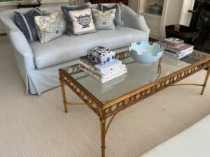 A living room featuring a pair of Niermann Weeks Tight Back Blue Sofas adorned with patterned pillows, accompanied by a glass-top coffee table displaying books, a decorative bowl, and a printed box.