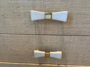 Two white and gold bow-shaped drawer handles resting on a pair of Niermann Weeks Tight Back Blue Sofas against a textured beige surface.