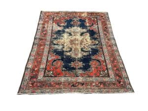 A vintage Persian rug with an intricate floral and geometric design in red, blue, and beige hues, featuring a central medallion and a detailed border.