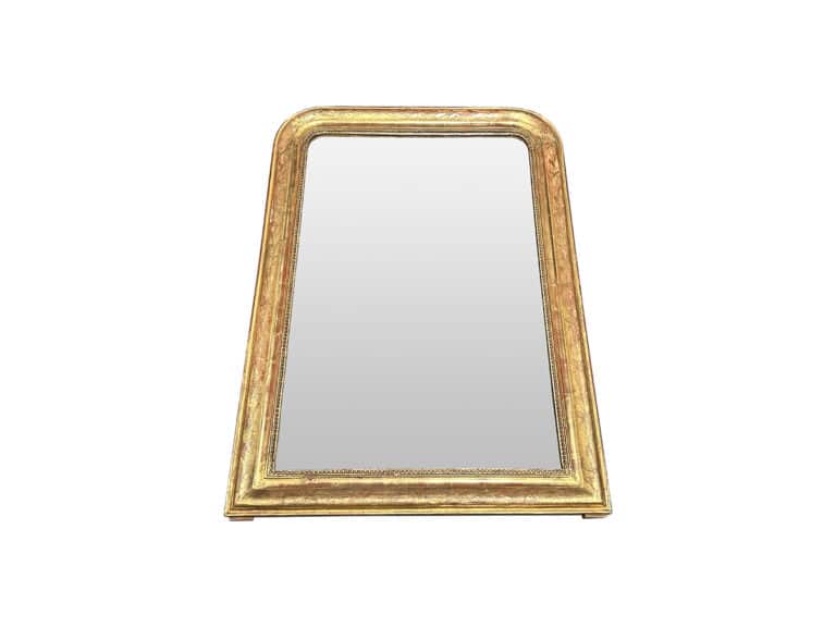 A trapezoidal gold-framed mirror with a reflective surface set against a white background.