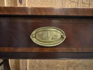 Close-up of a wooden drawer with an oval brass handle featuring a relief of a wheat sheaf design.