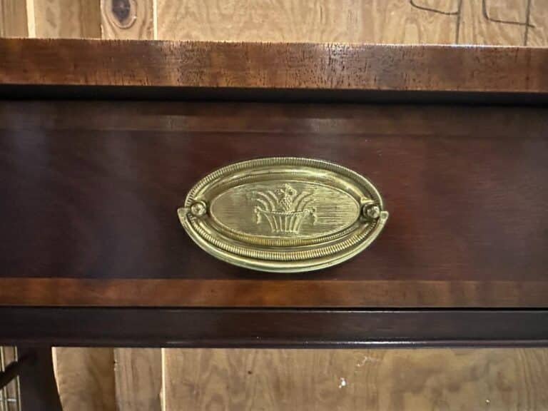 Close-up of a wooden drawer with an oval brass handle featuring a relief of a wheat sheaf design.