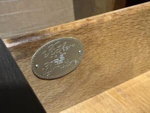 Metal plaque with "Baker Furniture" engraving on the inside of a wooden drawer.