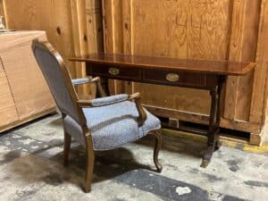 A wooden desk with two drawers and a cushioned chair are placed on a concrete floor in a storage area.