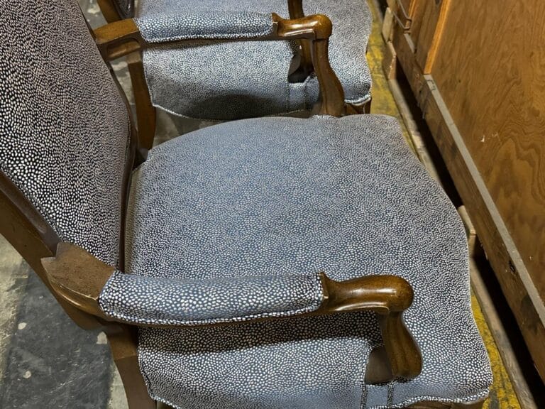 Close-up of two wooden chairs with speckled gray upholstery next to wooden furniture.