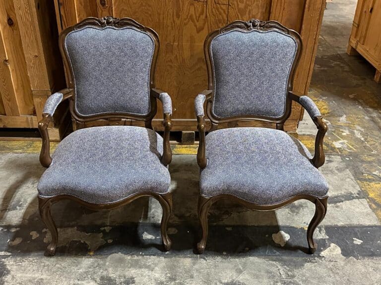 Two vintage chairs with carved wooden frames and upholstered seats and backs are positioned side by side on a concrete floor.