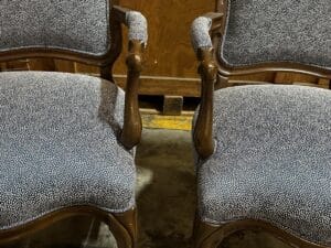 Two wooden chairs with curved armrests and gray, speckled upholstered seats and backs, placed on a concrete floor.