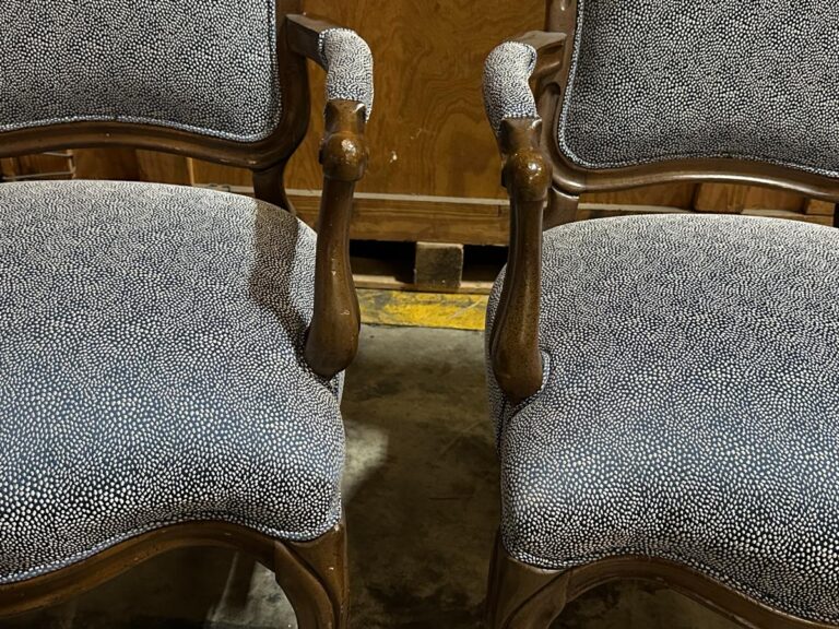 Two wooden chairs with curved armrests and gray, speckled upholstered seats and backs, placed on a concrete floor.