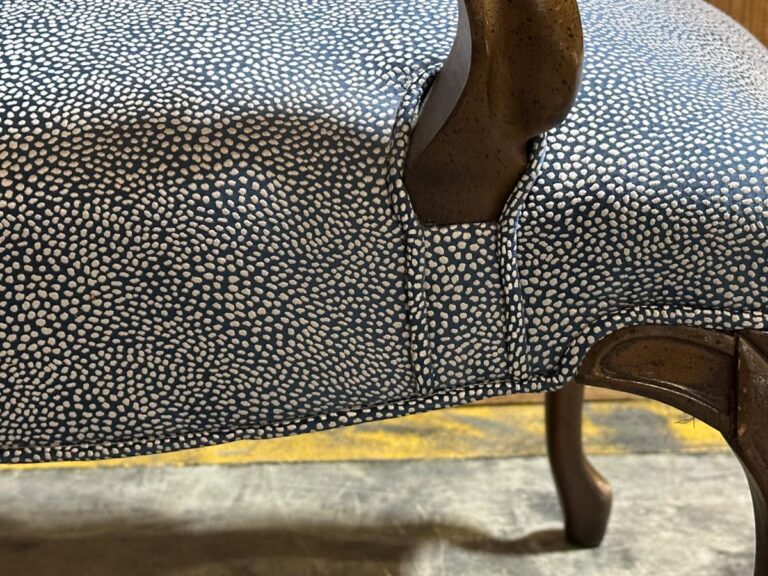 Close-up of a chair with textured, speckled upholstery in black and white, featuring a wooden armrest and leg.