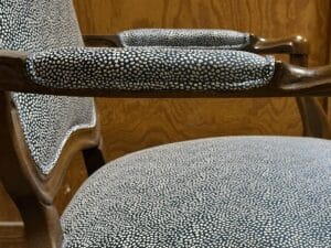 A wooden chair with armrests, featuring upholstery with a navy blue and white speckled pattern.