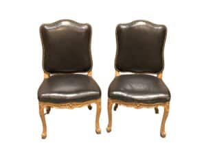 Two ornate chairs with black leather upholstery and gold-colored wooden frames, featuring decorative studs along the edges.