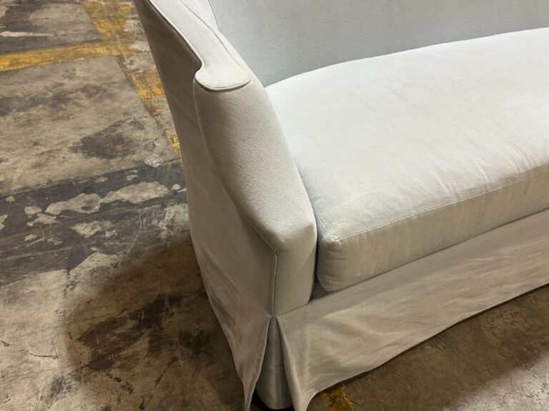 A light gray upholstered sofa is positioned on a concrete floor with visible cracks and lines.