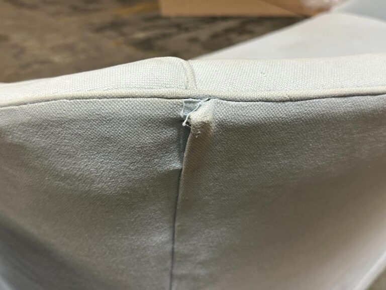 Close-up of a beige fabric seam with visible stitching and a small tear.