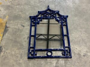 A blue ornate mirror with a geometric frame is placed on a concrete floor, reflecting a ceiling structure.