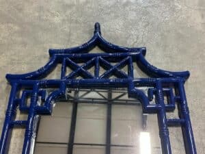 Decorative blue mirror with an architectural frame resembling a pagoda, placed on a concrete floor.