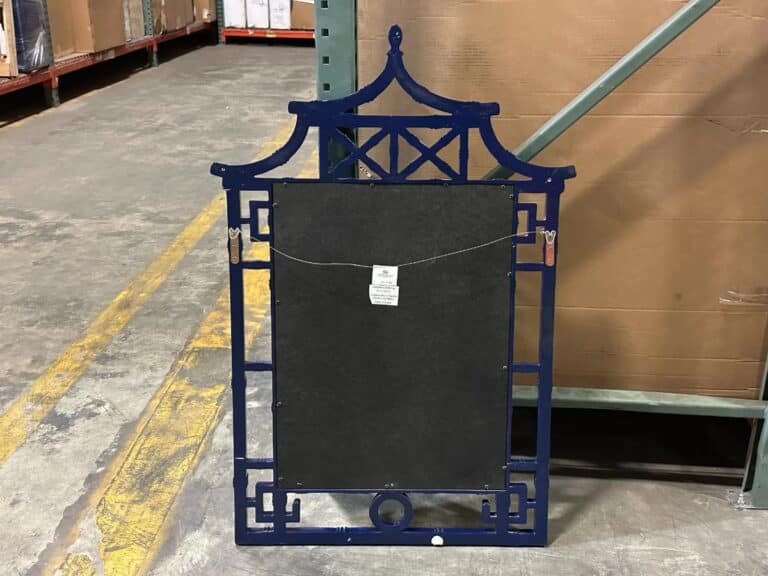 A decorative metal frame with an Asian-inspired design, featuring a black center panel and a small tag, is propped against a shelf in a warehouse.