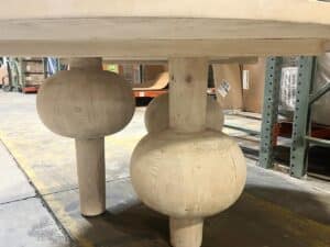 A close-up view of a wooden table with thick, round legs in a warehouse.