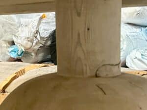 A collection of white and blue plastic bags and materials is seen in the background, partially obscured by a large wooden cylindrical object in the foreground.