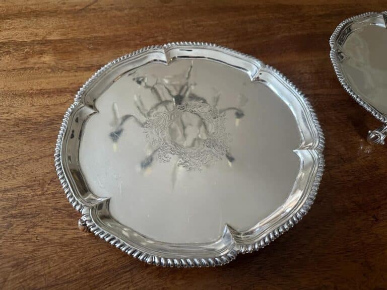 A polished silver tray with intricate floral engravings sits on a wooden surface.