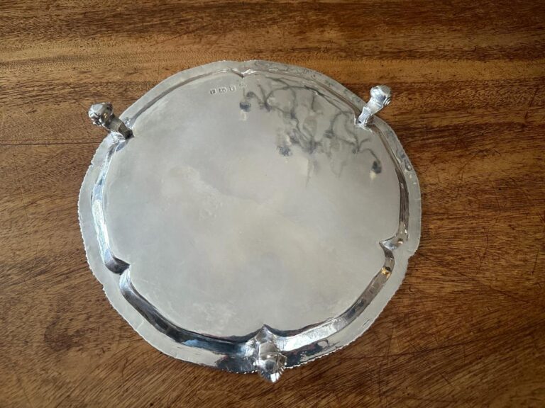 A silver plate with a scalloped edge and three small feet, resting on a wooden surface.