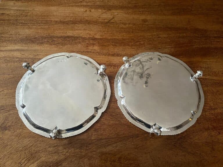 Two round silver platters with scalloped edges and small feet, placed on a wooden surface.