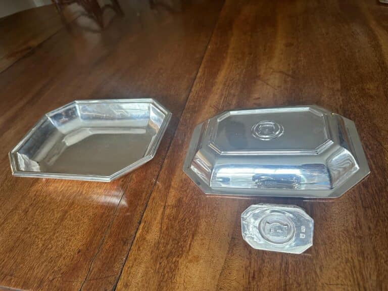 Silver serving dishes with an octagonal tray, a rectangular platter with lid, and a small octagonal lid on a wooden table.