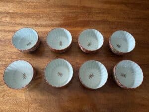 Eight decorative ceramic bowls with floral patterns arranged in two rows on a wooden table.