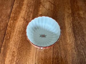 A small ceramic bowl with a scalloped edge and a floral design in the center sits on a wooden surface.