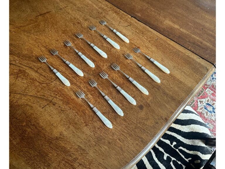 Fourteen small forks are arranged in neat rows on a wooden table with a zebra print rug partially visible below.