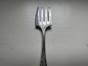 A silver fork with four decorative tines and an ornate handle on a light gray background.