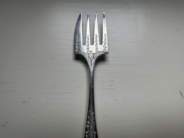 A silver fork with four decorative tines and an ornate handle on a light gray background.