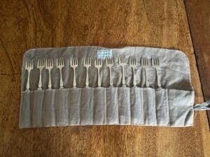 A set of nine silver forks neatly arranged in a canvas roll-up case on a wooden surface.