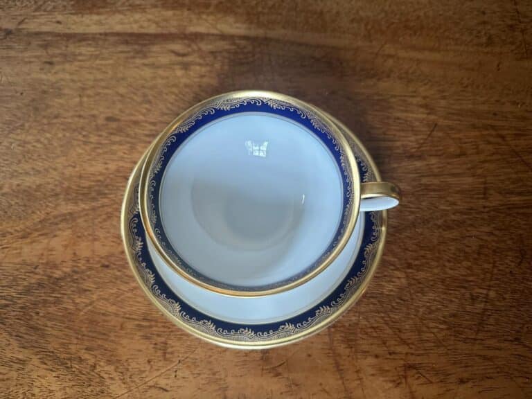 Aerial view of an ornate teacup and saucer with blue and gold trim on a wooden surface.