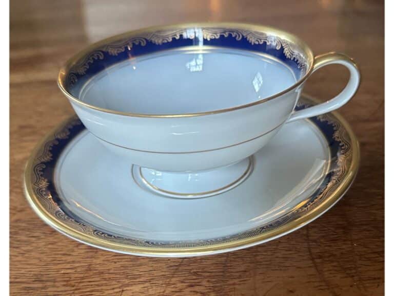 A porcelain teacup with saucer featuring a blue and gold rim design, placed on a wooden surface.