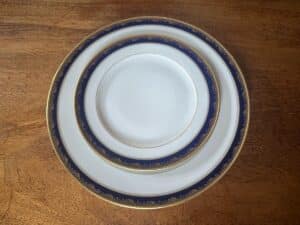 Three stacked white plates with blue and gold trim on a wooden table.