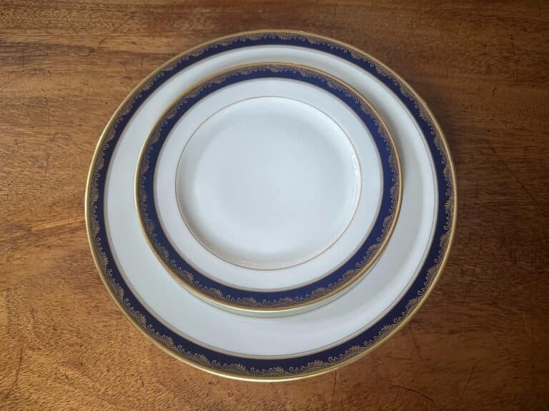 Three stacked white plates with blue and gold trim on a wooden table.